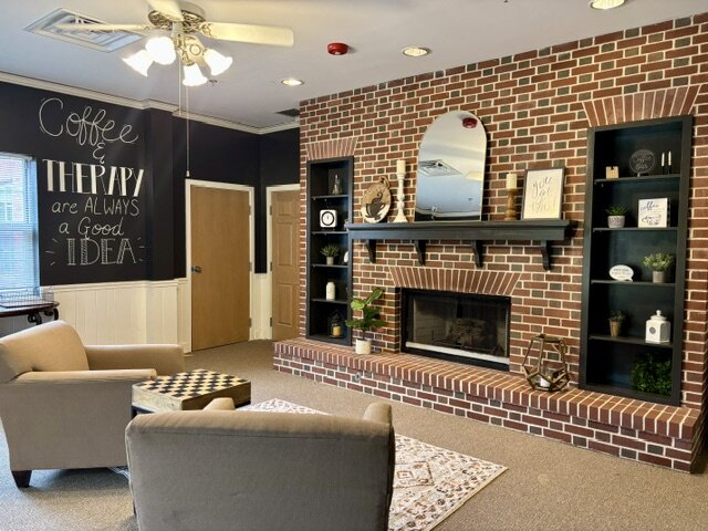 Homey living room with a fireplace and a 'Coffee & Therapy' sign at Fostering Change